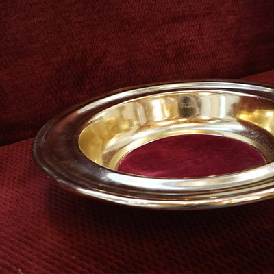 Gold offering plate with red velvet lining on red velvet church pew